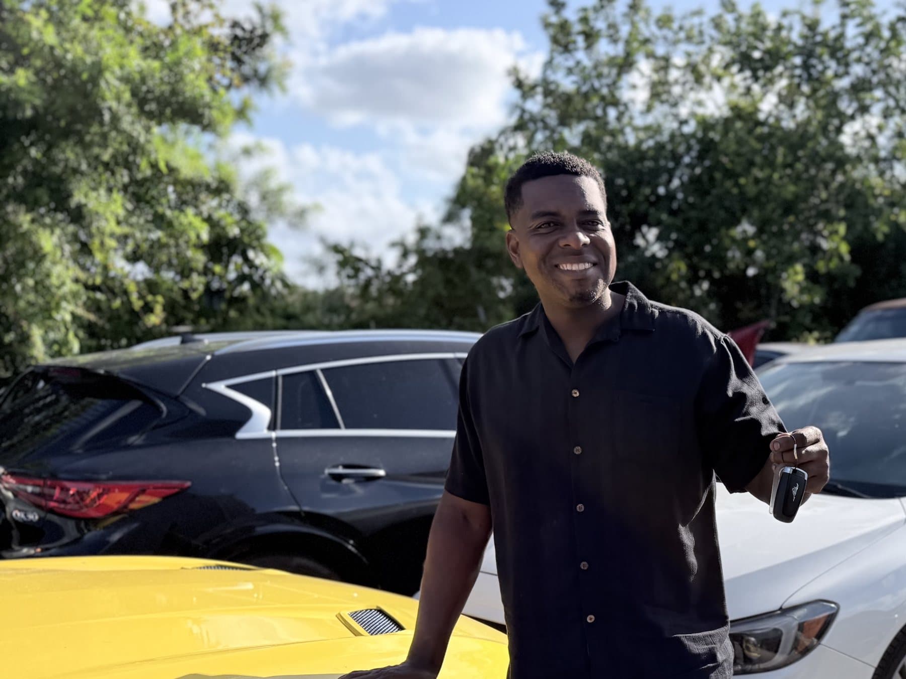 Omari Grant, ASE-certified mechanic and owner of Fort Lauderdale Auto Sales, holding keys beside inspected inventory